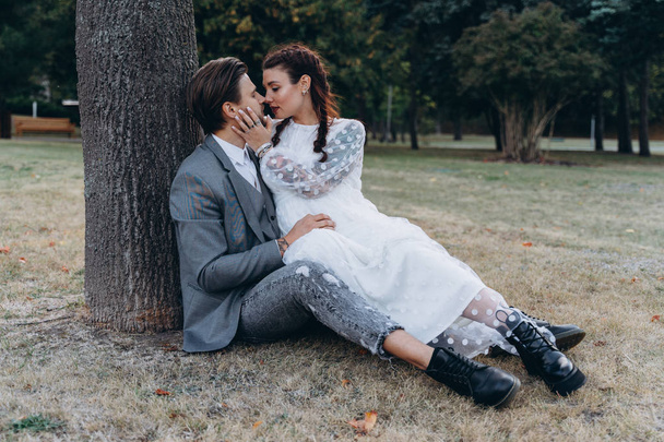 beautiful pregnant woman in white dress with handsome man sitting on the ground near a tree trunk - Fotografie, Obrázek