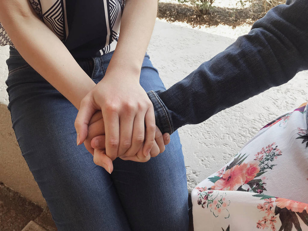 nuoret naiset pitävät toisiaan kädestä lohdutukseksi
 - Valokuva, kuva
