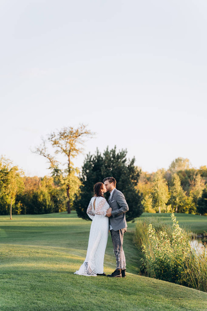 beautiful pregnant woman in white dress with handsome man kissing at green lawn in evening - Foto, Imagen