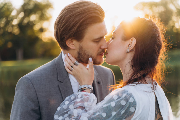 beautiful pregnant woman in white dress with handsome man kissing at green lawn against the setting sun - Valokuva, kuva