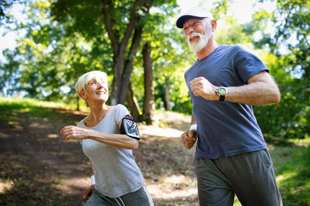 Mature or senior couple doing sport outdoors, running in a park - 写真・画像