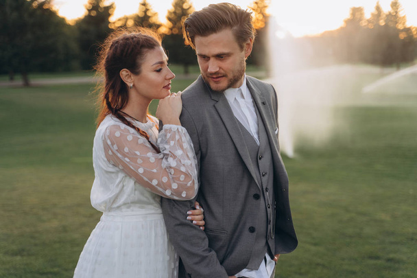beautiful pregnant woman in white dress with handsome man while watering the lawn in evening - Valokuva, kuva