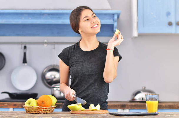 A young asian woman in a black t-shirt makes a fit breakfast and tries to taste a piece of apple. - Foto, Imagen