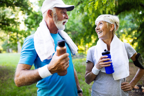 Beautiful senior couple running outside in sunny forest - Photo, image