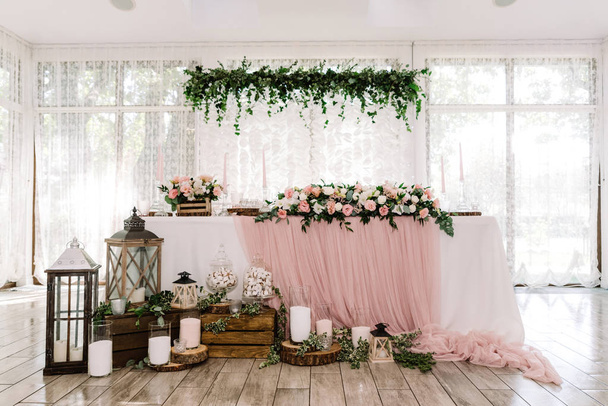Bela mesa de noivo e noiva perto de grandes janelas de luz decoradas com materiais naturais
 - Foto, Imagem