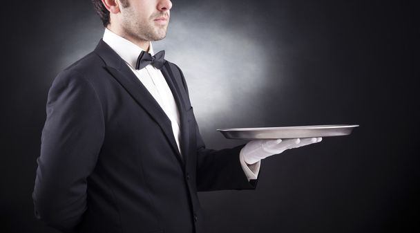 Waiter holding empty silver tray over black background - Foto, Imagen