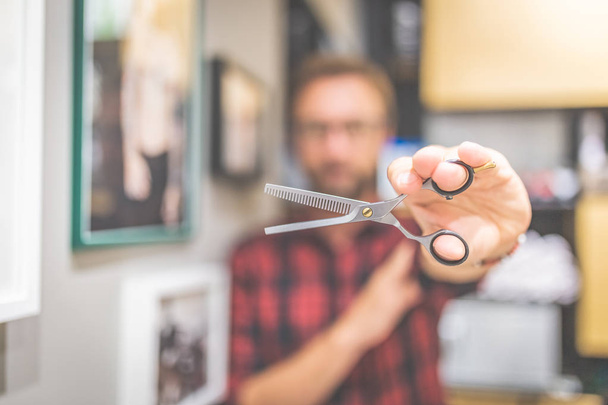Modern man hairdresser holding sharp professional scissors at barbershop. - 写真・画像