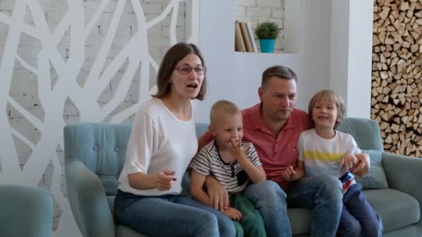 Excited family football fans watching tv, celebrating goal together, happy parents mom dad and little kids supporting favorite soccer team victory at home sit on sofa - Imágenes, Vídeo