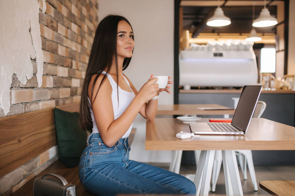 Mujer joven bebiendo café y trabajando en el ordenador portátil en la cafetería. Mujer inteligente ganar dinero en línea. Estudio de estudiantes en cafetería
 - Foto, imagen