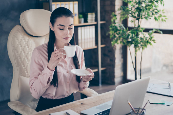 Photo of dreamy cheerful resting marketer holding cup of warm beverage with her hands eyes closed with rejocing at desktop with computer on it - Foto, Bild