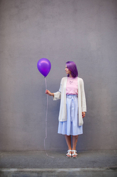 Girl with purple hair standing in front of gray wall and hold airballoon - Foto, afbeelding