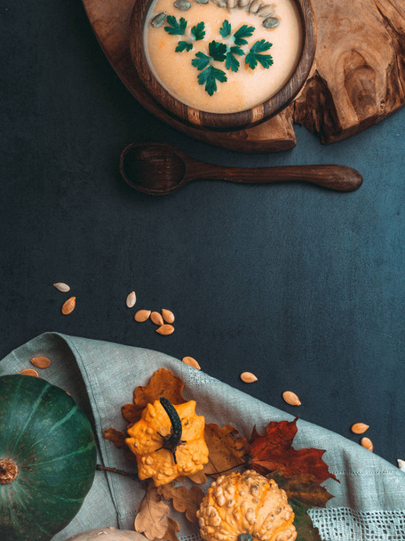 hot yellow pumpkin and lentils soup, with seeds, parsley in oak wooden bowl, spoon from wood, decorative autumn foliage on kitchen linen towel, healthy food concept - Foto, Imagem