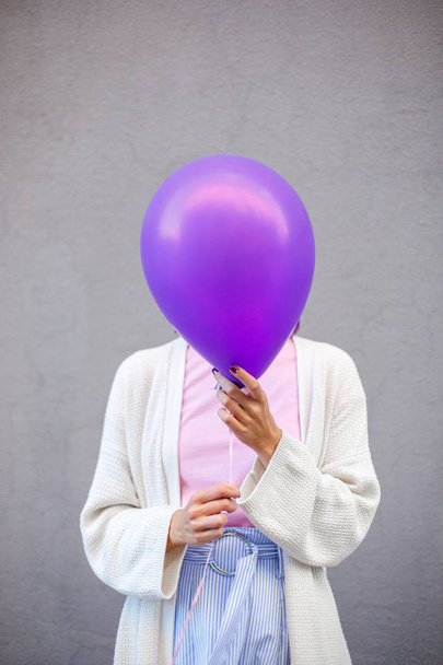 Γυναίκα με λευκό πουλόβερ καλύπτει το κεφάλι της με ένα μωβ μπαλόνι - Φωτογραφία, εικόνα