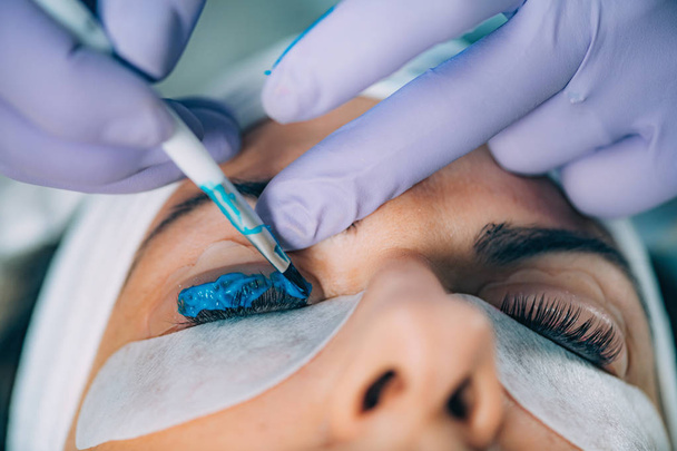 Cosmetoloog zet blauwe verf op de wimpers tijdens het opheffen van de lash-procedure. Lamineren van wimpers.  - Foto, afbeelding
