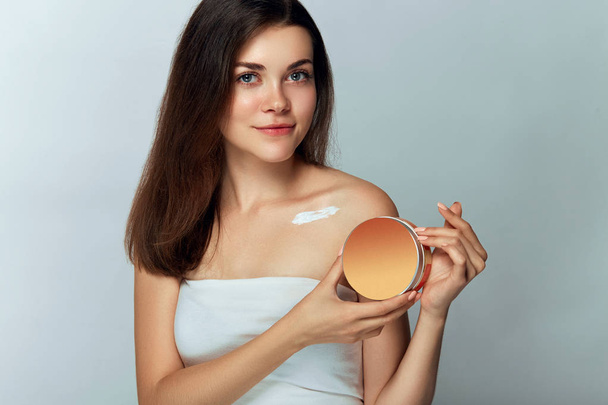 Beauty Concept. Woman Holds a Cosmetic Crem in her Hand and Spreads it on Her Shoulder  to Moisturize her Skin. Female Applying Cream and Smiling. Beauty Face.  Body Care, Skincare. - Fotó, kép