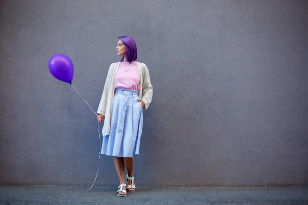 Female violet hair standing with purple airballoon in front of gray background - Фото, зображення