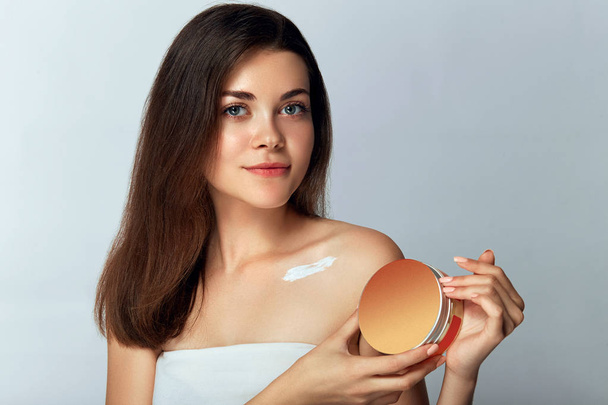 Beauty Concept. Woman Holds a Cosmetic Crem in her Hand and Spreads it on Her Shoulder  to Moisturize her Skin. Female Applying Cream and Smiling. Beauty Face.  Body Care, Skincare. - Valokuva, kuva