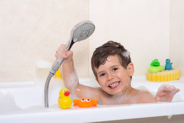 Гигиена для младенца и ребенка. Ребенок играет с мыльной пеной в домашней ванной. Резиновая утка в пенной ванне
.  - Фото, изображение