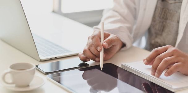 Foto recortada de jovem freelancer do sexo masculino escrevendo em tablet enquanto trabalhava em seu projeto em seu moderno escritório
  - Foto, Imagem