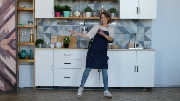 Pretty young woman dancing in the kitchen and listening music. - Záběry, video