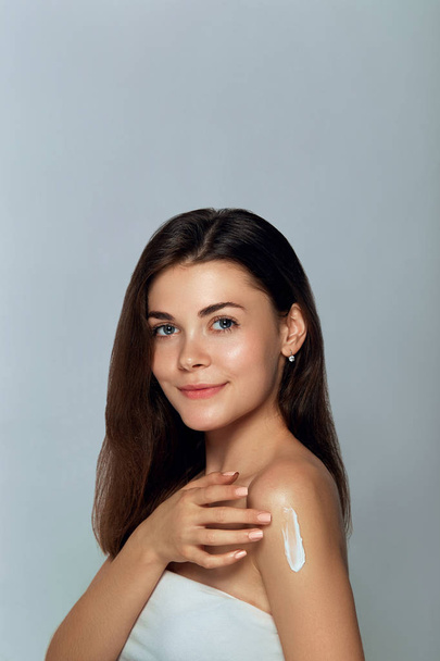 Beauty Concept. Woman Applying  Cosmetics Cream and Smiling. Female holds a   bottle  crem in her hand and spreads it on her shoulder  to moisturize her skin. Beauty Face. Body care. Skincare. - Photo, Image