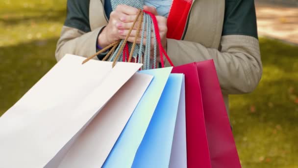 Een jonge vrouw in een jasje is aan het winkelen. Een meisje staat in het park met aankopen in veelkleurige papieren tassen. Verkoop, retail industrie concept. Een close-up. 4k-beelden. - Video