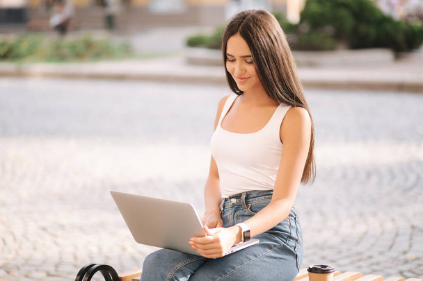 Attractive young woman in use laptop outside on the banch in summer time. Beautiful brunette female Student study - Φωτογραφία, εικόνα