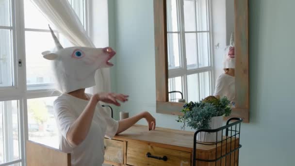 Strange funny video: woman in a mask of unicorn looking in the mirror in bedroom - Кадры, видео