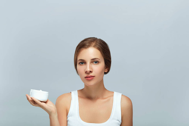 Beauty Concept. Taking good care of her skin. Attractive young woman looking at camera.Portrait of attractive female with healthy smooth facial clean skin holding bottle. Face Skin Care. - Фото, зображення