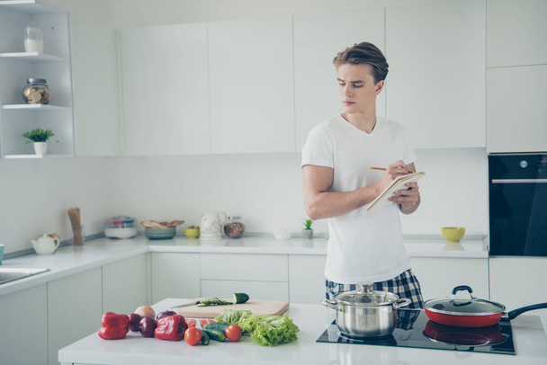 Portrait of his he nice attractive serious focused guy learning making lunch writing notes plan buyings at light white modern style interior house indoors - Foto, Imagem