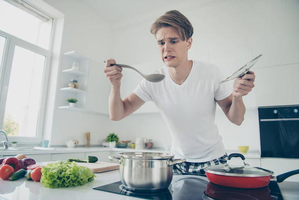 Portrait of his he nice attractive cute dissatisfied upset guy making dinner lunch tasting bad bouillon at light white modern style interior house indoors - Zdjęcie, obraz