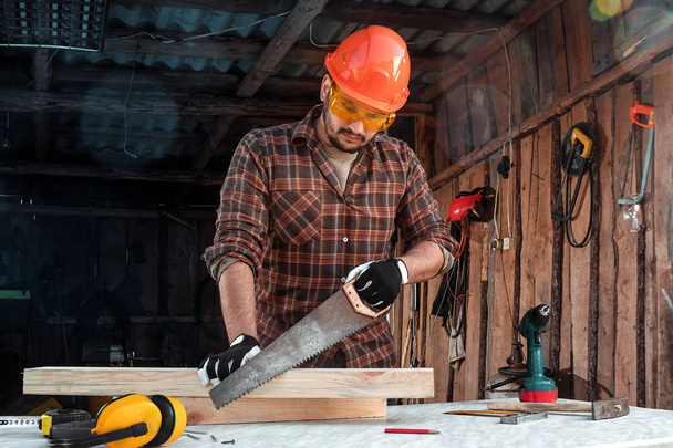 A man carpenter cuts a wooden beam using a handsaw, male hands with a saw closeup. Work with wood. - Photo, image