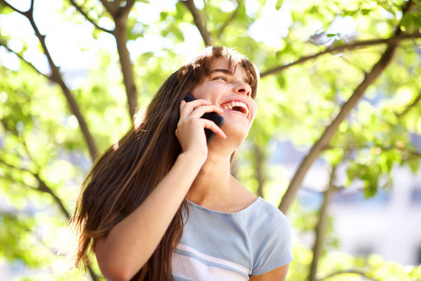 Close up portrait of beautiful smiling young woman talking with mobile phone in park - Photo, image