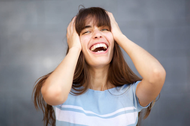 Close up portrait of young woman long hair laughing with hands in hair against gray background - Foto, afbeelding