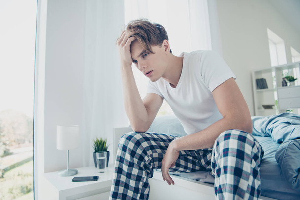 Portrait of unhappy unwell man after hangover party suffer terrible migraine have cold inflammation horrible pressure sit on bed wear plaid checkered pajama in house indoors - Фото, изображение