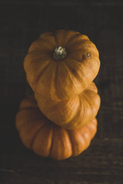 Orange littlep pumpkins on dark wooden background deep shadows, rustic style halloween, thanksgiving, autumn - Foto, afbeelding