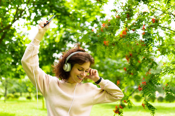 Genç ve güzel bir kadın bahçede müzik dinliyor.  - Fotoğraf, Görsel