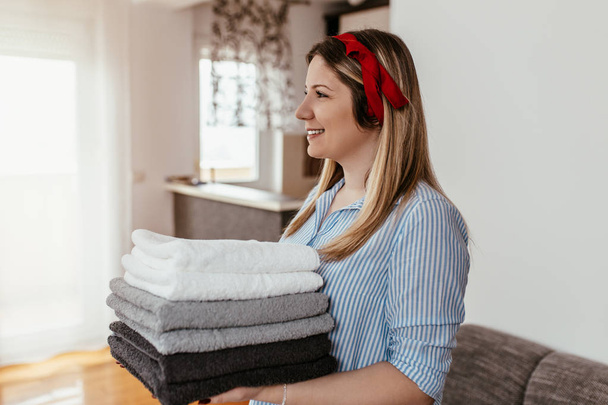 Young woman holding a pile of ironed clean towels. - Photo, Image