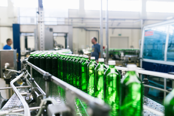 Water factory - Water bottling line for processing and bottling pure mineral water into green glass bottles. Selective focus. - Photo, Image
