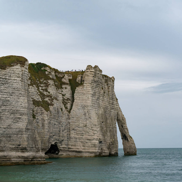  tourists enjoy hiking on the Normandy coast along the Falaise de Etretat cliffs above the village of Etretat - Foto, Imagen