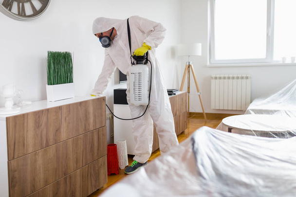 Kammerjäger in Arbeitskleidung versprüht Pestizid mit Sprüher.  - Foto, Bild