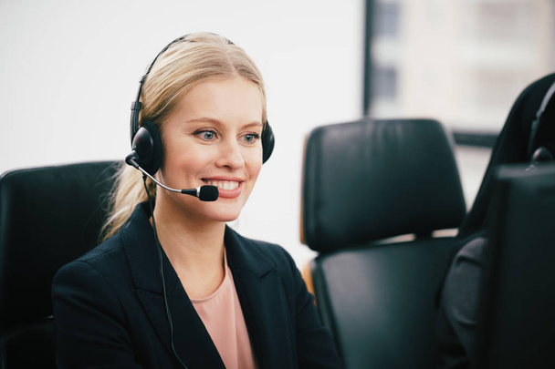 A smiling  beautiful woman sitting in a customer service department office with headset working in call center - 写真・画像