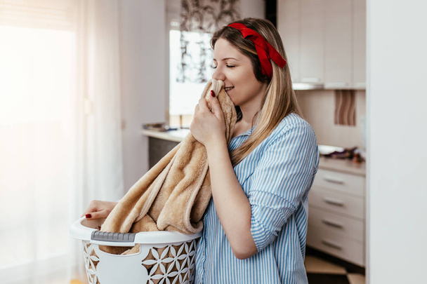 Красива молода усміхнена жінка пахне чистими рушниками під час прання вдома
. - Фото, зображення