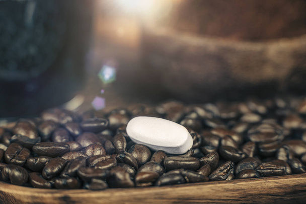 Caffeine pill and roasted coffee beans with grounded coffee in wooden bowl in background - Photo, Image
