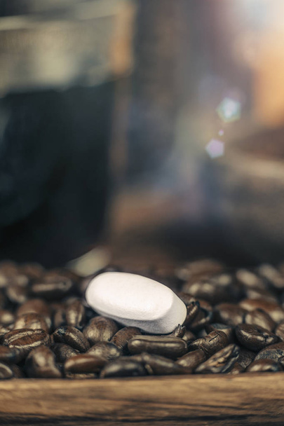 Caffeine pill and roasted coffee beans with grounded coffee in wooden bowl in background - Photo, Image