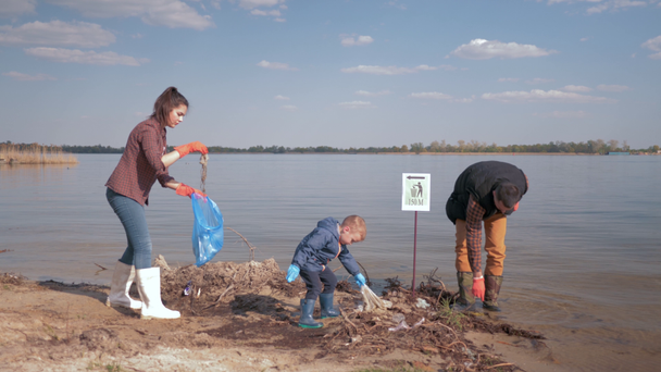 environmental solutions, child boy helps mother and father volunteer activists clean up dirty river shore from plastic trash and collected in garbage bag saving ecology nature - Footage, Video