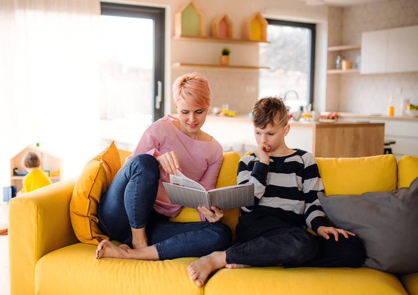 Une jeune femme avec un fils à l'intérieur à la maison, lisant un livre
. - Photo, image