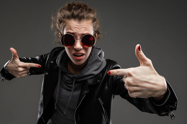 fashionable young woman posing in leather jacket and sunglasses against dark background - Foto, immagini