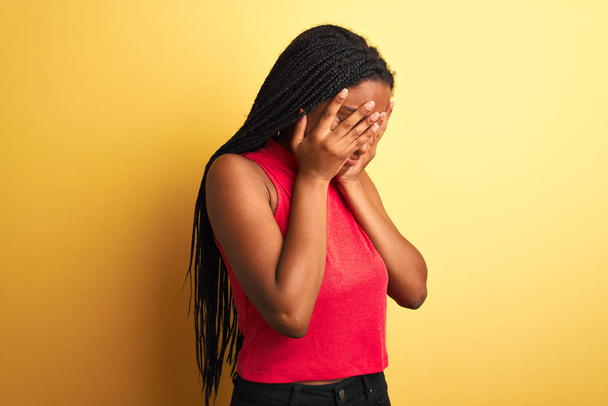 Afrikkalainen amerikkalainen nainen yllään punainen rento t-paita seisoo yli eristetty keltainen tausta surullinen ilme peittää kasvot kädet itkien. Masennuksen käsite
. - Valokuva, kuva