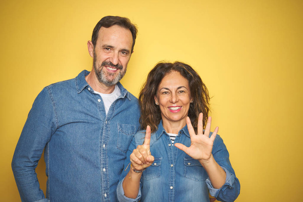 Bella coppia di mezza età insieme in piedi sopra isolato sfondo giallo mostrando e indicando con le dita numero sei, sorridendo fiducioso e felice
. - Foto, immagini